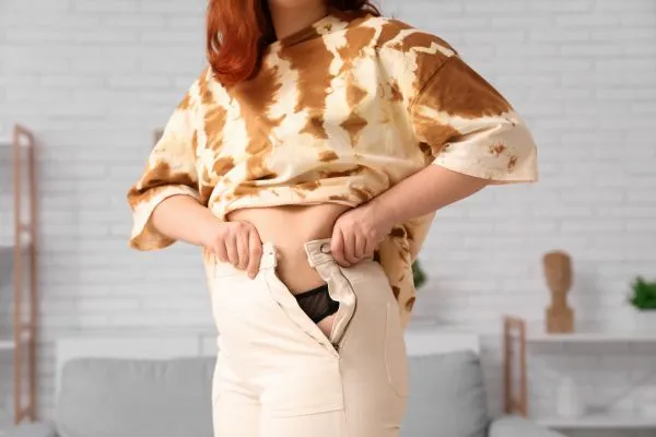 Image of woman trying to do her trousers up after pregnancy weight gain Dunmow